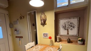 Un coin repas avec une table et des chaises en bois, un luminaire suspendu, une statue de Bouddha et une œuvre d’art encadrée accrochée au mur.