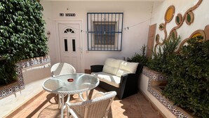 Une terrasse extérieure avec une table ronde en verre, des chaises en osier, un canapé blanc et une porte portant l’inscription « LA CUEVA ».