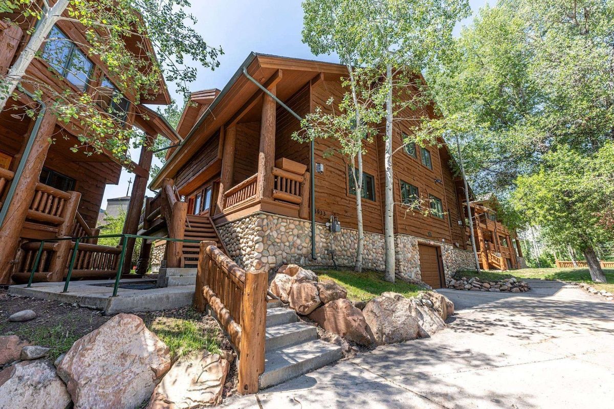 A wooden cabin with a stone foundation, a balcony, and a stone pathway leading to the entrance.