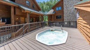 Una cabaña de madera con jacuzzi en una terraza, paredes de piedra y un porche cubierto.
