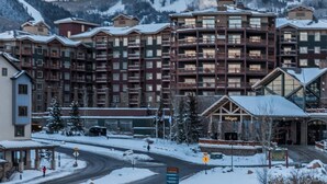 Un hotel de varios pisos con balcones, una estación de esquí al fondo y un cartel que dice 'Summit'.