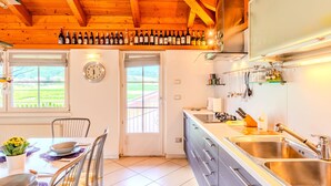 Una cocina moderna con vigas de madera, un área de comedor con una mesa dispuesta para dos personas, y vistas al exterior a través de una ventana.