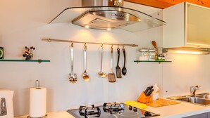 Una cocina moderna con estufa a gas, utensilios colgantes y una campana extractora de acero inoxidable.
