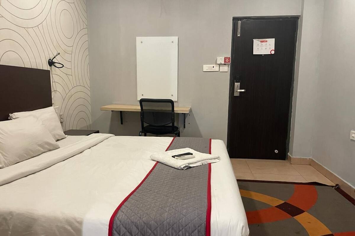 A hotel room with a bed, a desk, a chair, and a door.