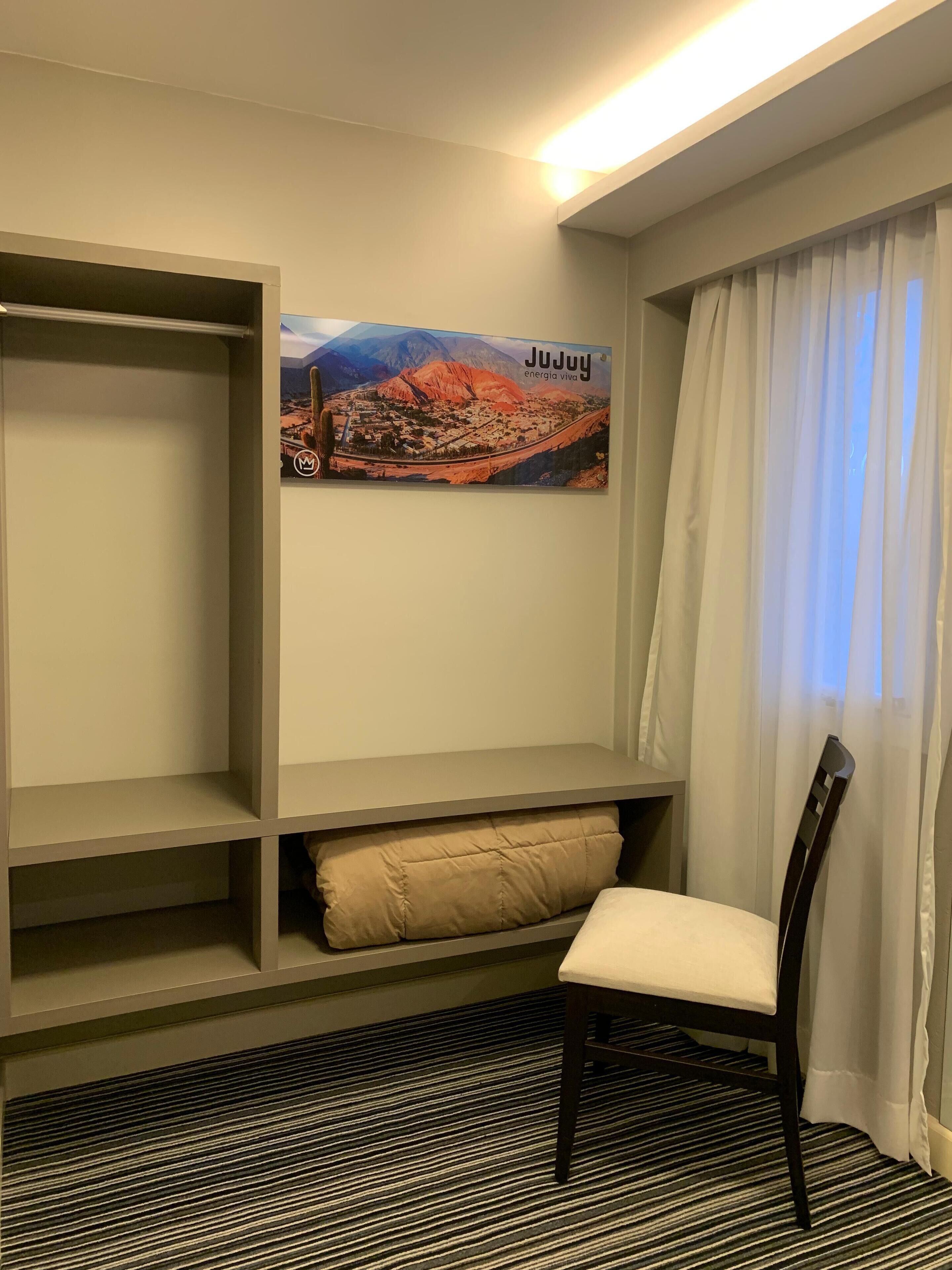 A room with a bed, a chair, a shelf unit, and a poster on the wall.