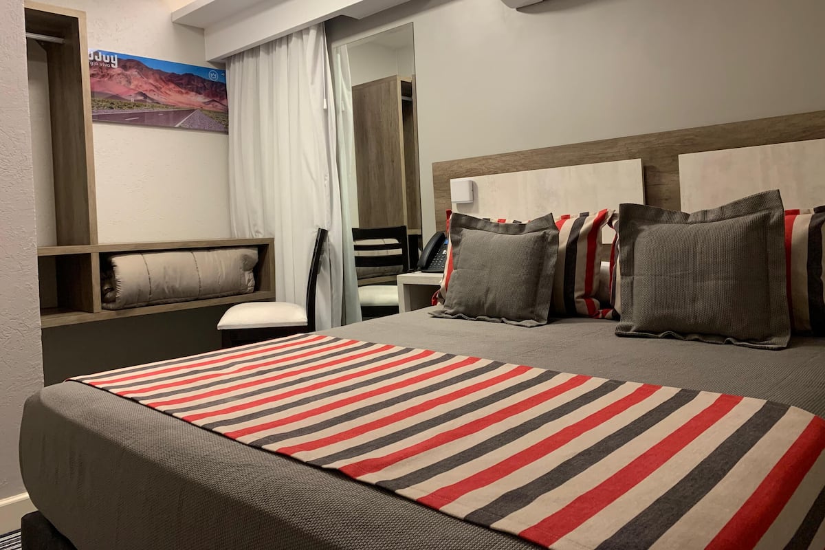 Habitación de hotel con cama, escritorio, silla, teléfono y aire acondicionado instalado en la pared.