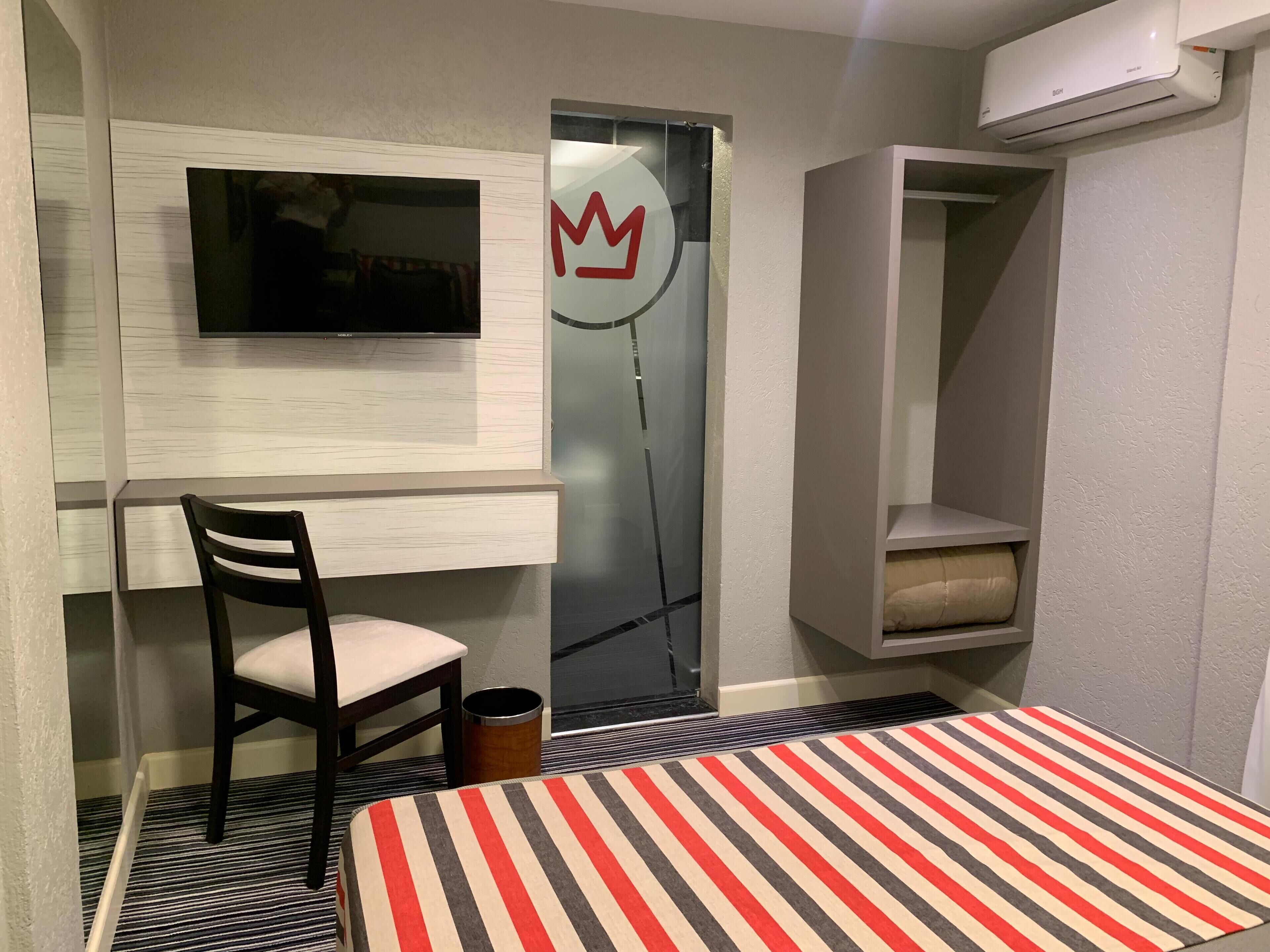 A compact room with a bed, a chair, a TV mounted on the wall, and a wardrobe.