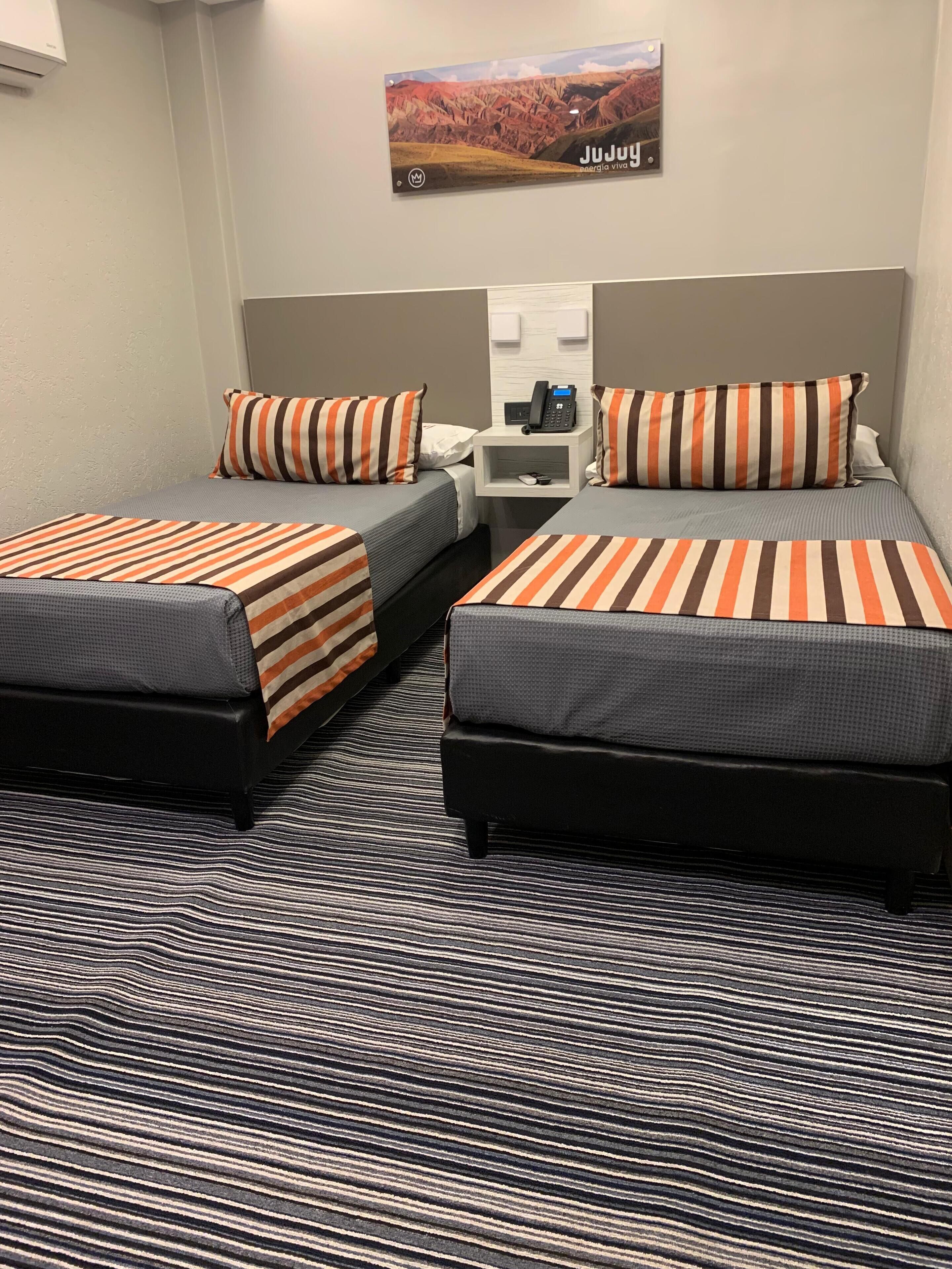 A hotel room with two beds, striped bedding, a nightstand with a phone, and a wall-mounted picture.
