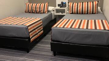 A hotel room with two beds, striped bedding, a nightstand with a phone, and a wall-mounted picture.