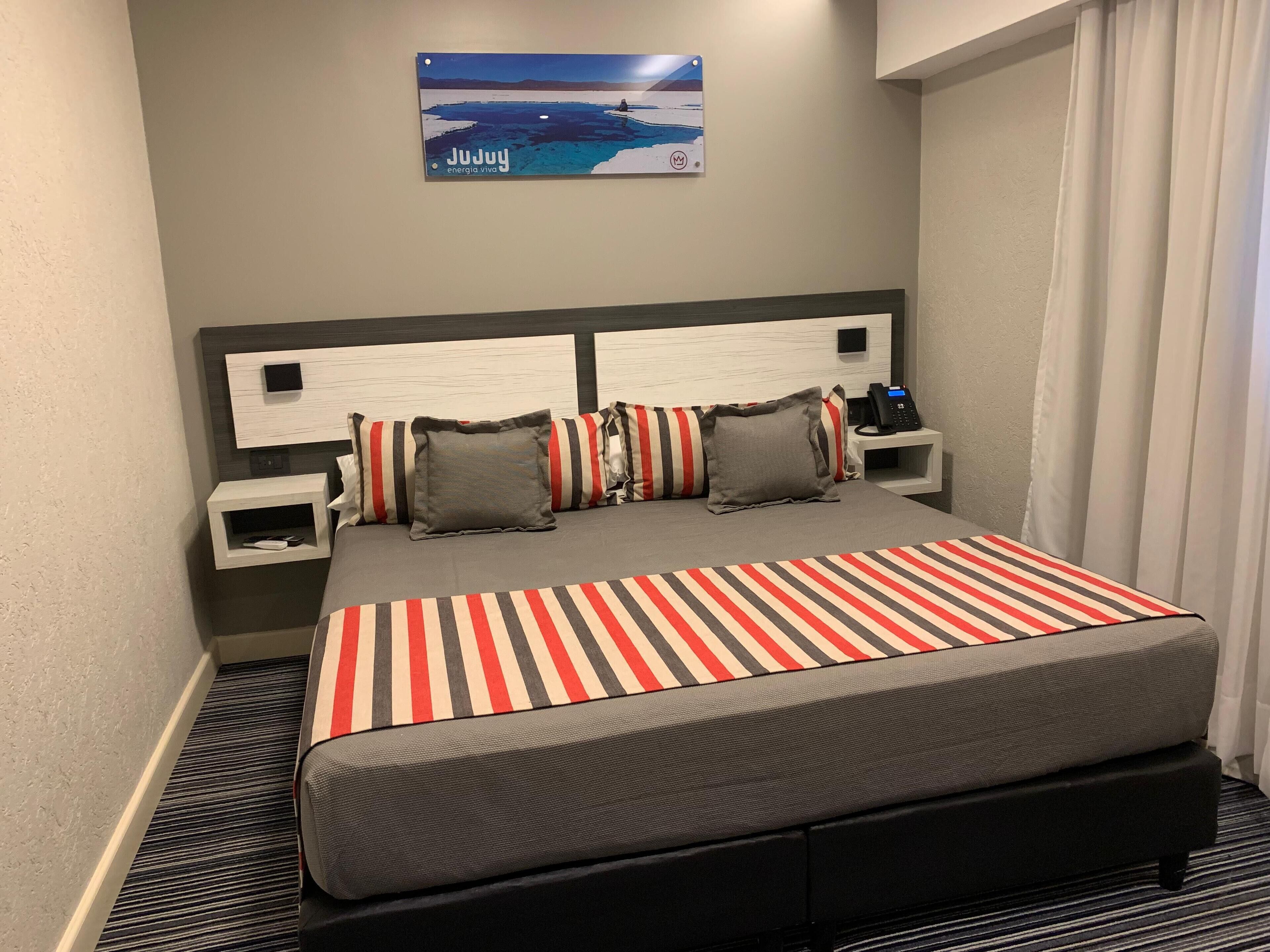 A hotel room with a bed, striped bedspread, and a nightstand with a phone.