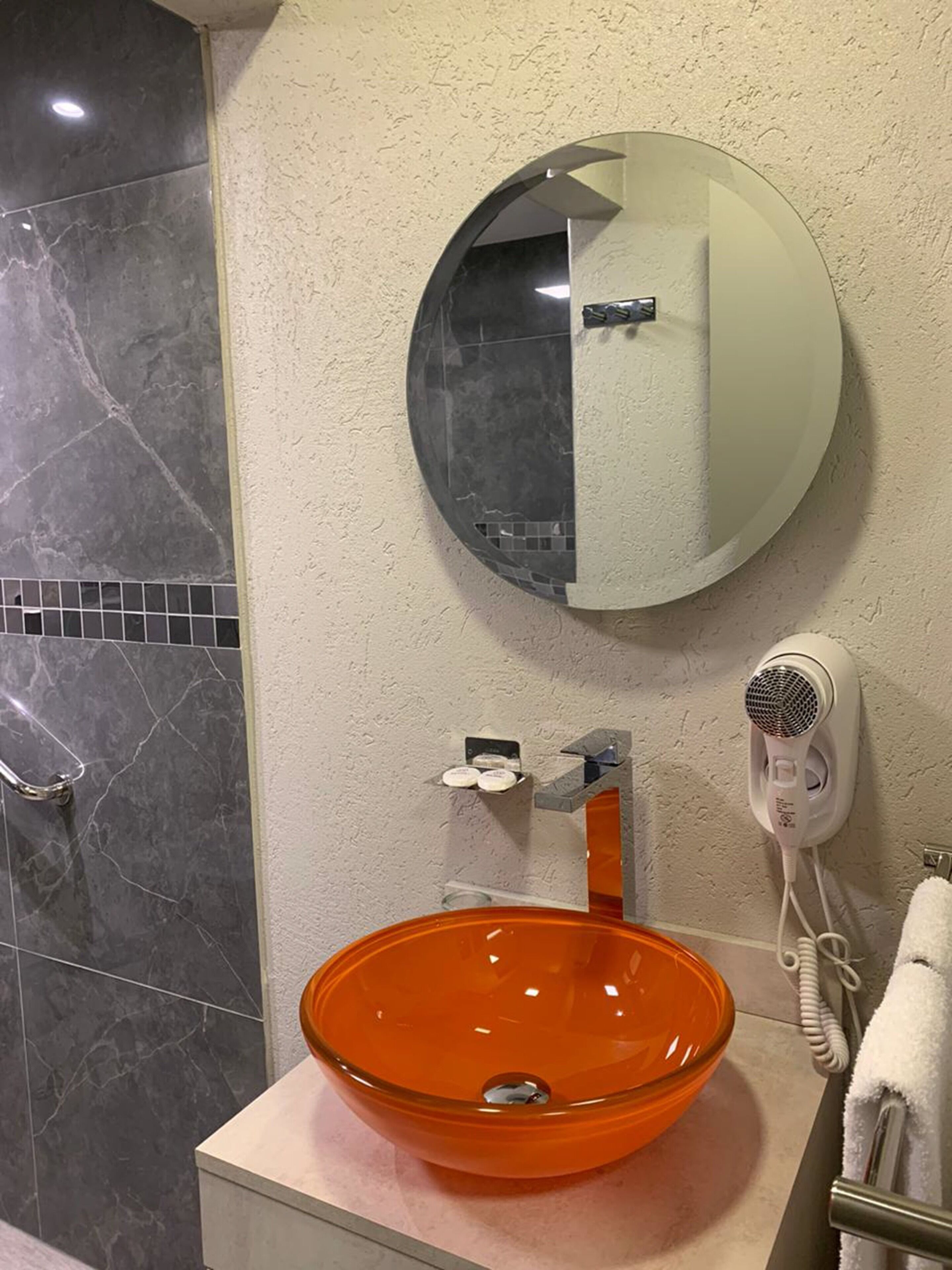 Un baño con un espejo redondo, un lavabo de cristal, un secador de pelo y una zona de ducha.