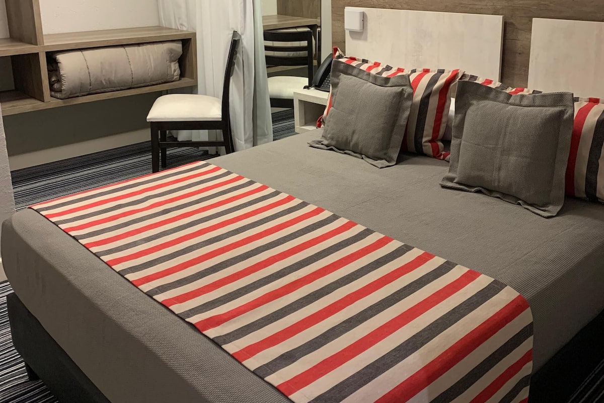 Habitación de hotel con cama, mesita de noche, silla y aire acondicionado instalado.