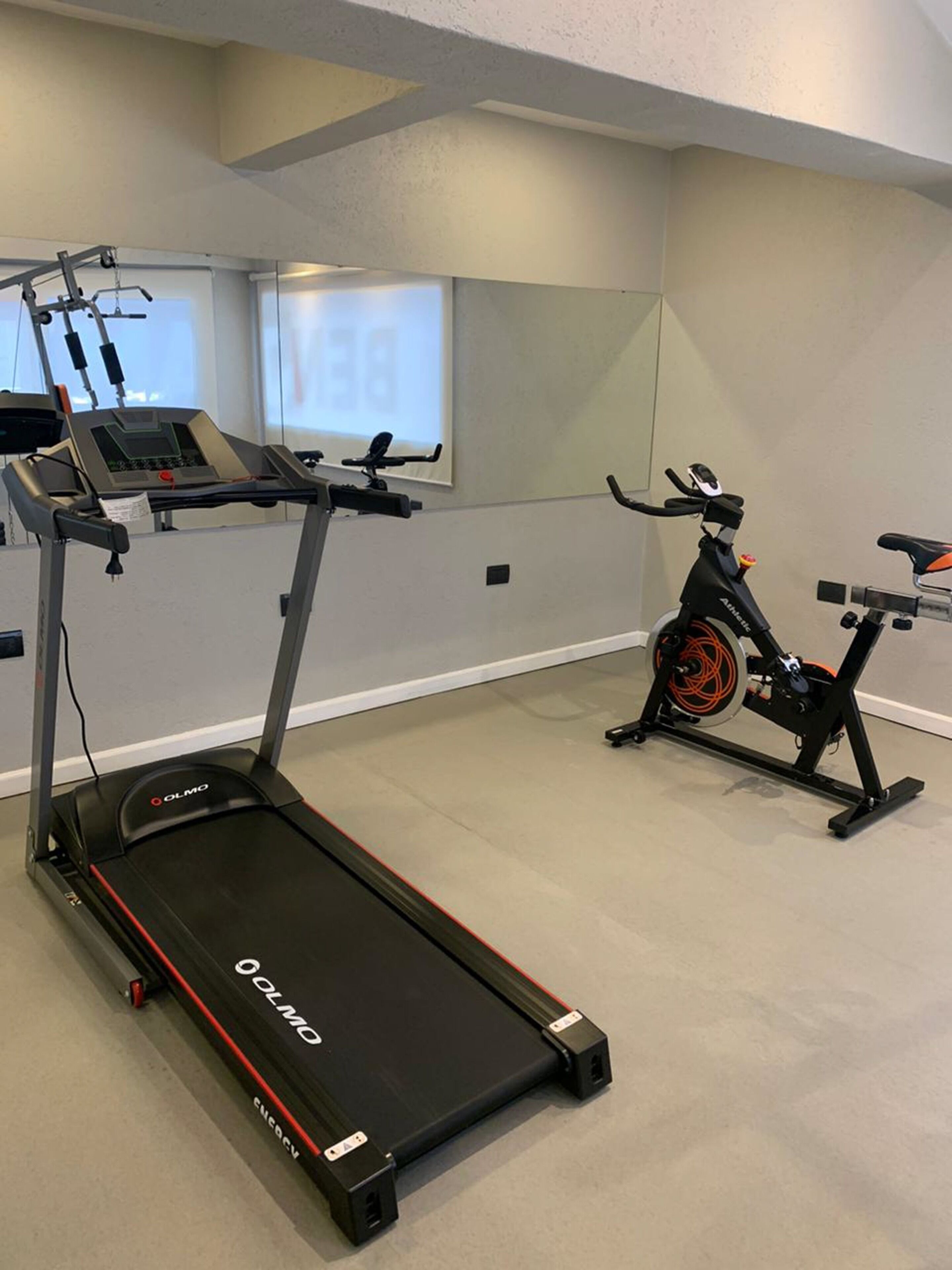 A gym with a treadmill, an exercise bike, and a wall-mounted screen.