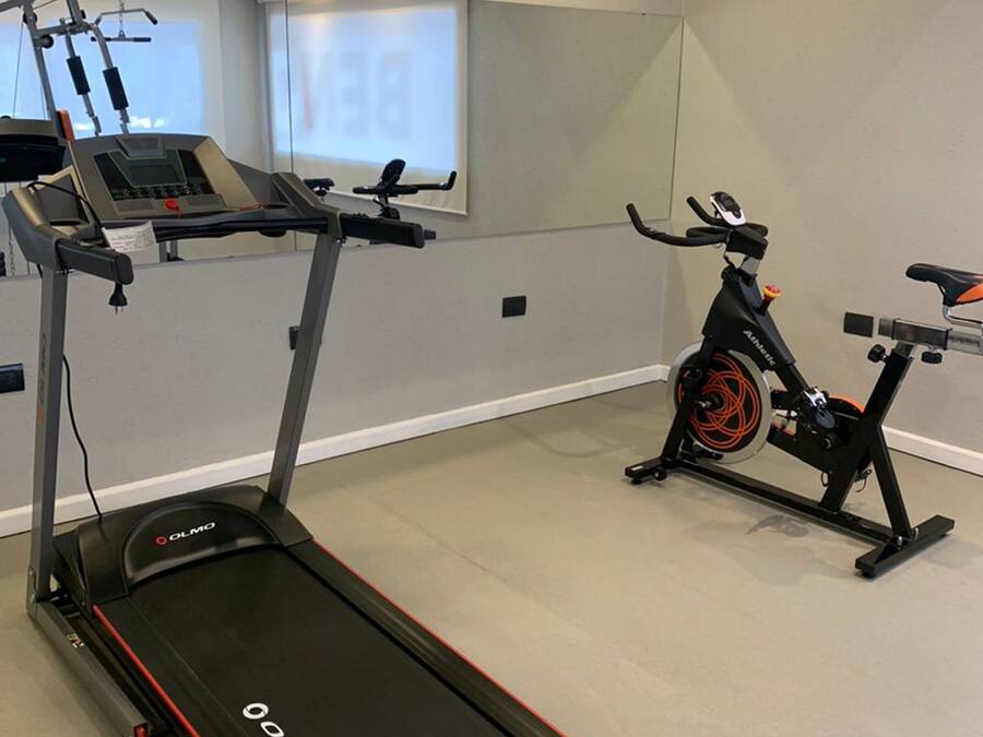 A gym with a treadmill, an exercise bike, and a wall-mounted screen.
