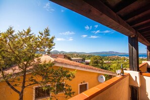 Ein Balkon mit Blick auf das Meer, einen Baum und ein Gebäude mit gelber Fassade.