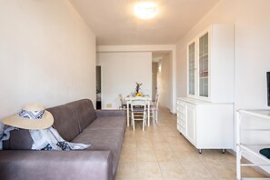 Ein Wohnzimmer mit einer Couch, einem Esstisch mit Stühlen, einem Schrank und einem Fernseher auf einem Schrank.