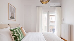 Et soveværelse med en seng, hvide gardiner, en radiator og et billede i ramme på væggen.