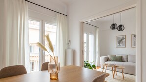 Et spiseområde med et træbord, stole og en vase med pampasgræs. En sofa og et lille bord ses i baggrunden.