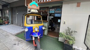 Un tuk-tuk estacionado frente a un edificio con un letrero que dice 'homies Bangkok'.