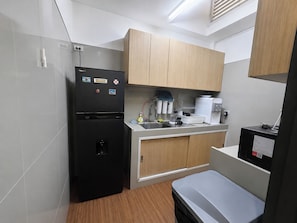 A compact kitchen with a black refrigerator, wooden cabinets, a white countertop, and a small sink. - Homies Ratchada Hotel (Bangkok)
