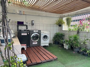 A laundry area with two washing machines, a drying rack, and potted plants. - Homies Ratchada Hotel (Bangkok)
