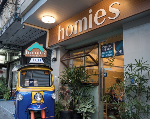 A taxi parked in front of a building with a sign that reads "homies" and a "Room for Rent" sign.
