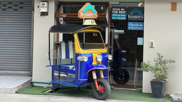 Un tuk-tuk estacionado frente a un edificio con un letrero que dice 'homies'.
