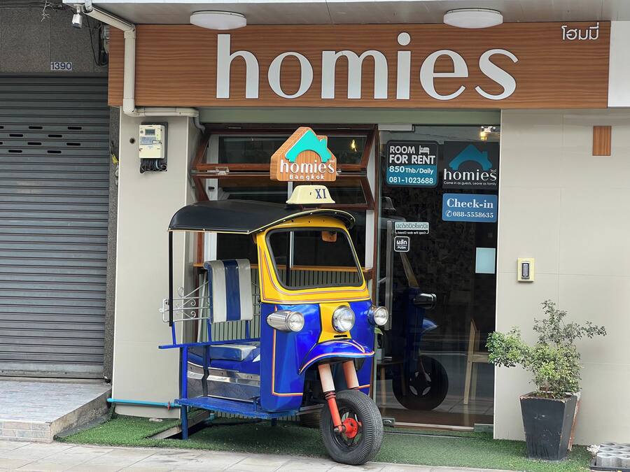 Um tuk-tuk estacionado em frente a um prédio com uma placa que diz 'homies'.