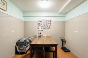 Quarto com mesa de madeira, caixa de transporte para animais de estimação, um pôster e uma tomada na parede.