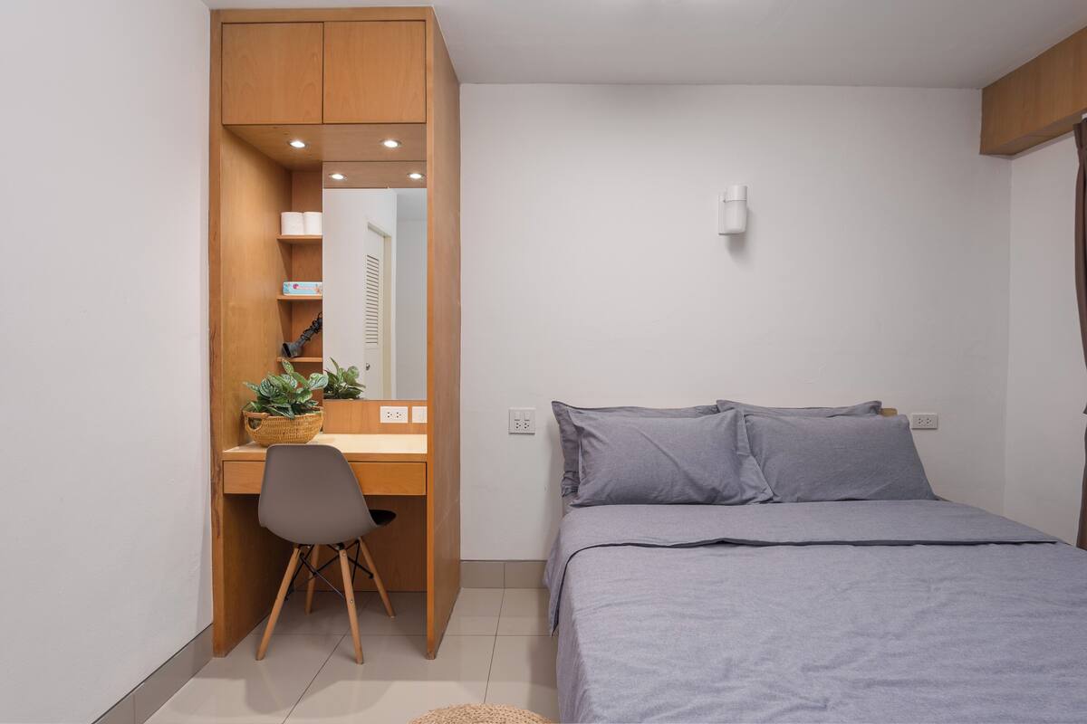 A bedroom with a bed, a desk with a chair, a small plant, and a mirror.