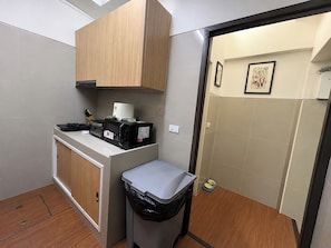 A compact kitchenette with a microwave, toaster, and coffee maker, a trash bin, and a small pet feeding station. - Homies Ratchada Hotel (Bangkok)