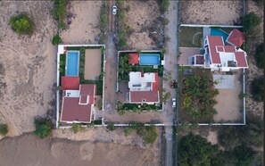 An aerial view of a coastal residential area with houses, a swimming pool, and a beach.