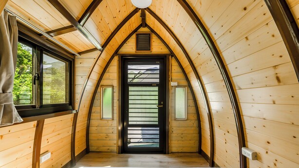 A cozy, triangular wooden room with a bed, a window, and a door with a view of greenery outside. - NA SUN NA GU (Nan-ao)