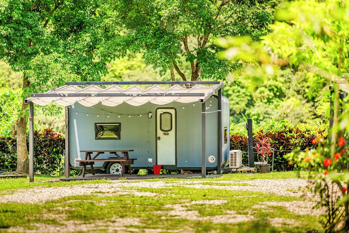 A small, single-room RV with a covered porch, a picnic table, and a small window.
