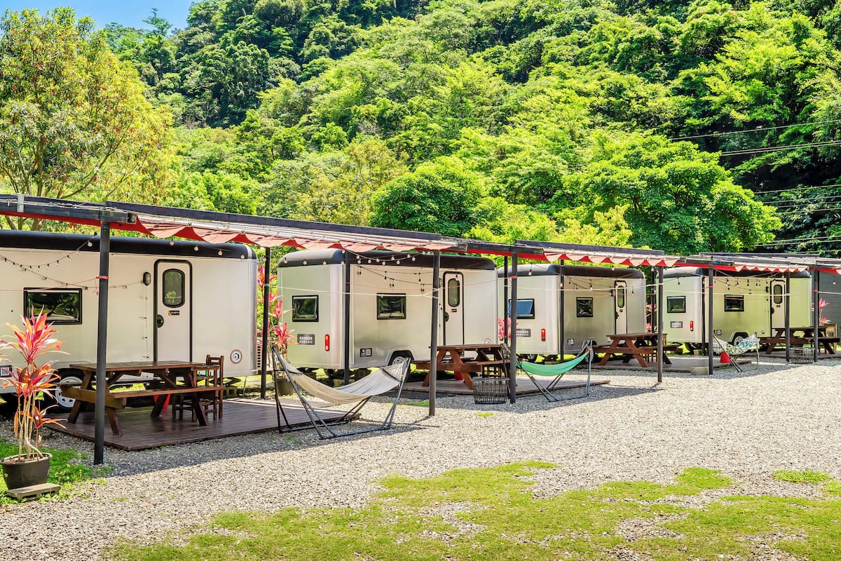 A row of RVs with picnic tables and hammocks, set against a backdrop of lush greenery.