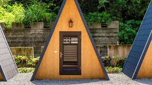 A triangular wooden structure with a door and a lantern, surrounded by greenery. - NA SUN NA GU (Nan-ao)
