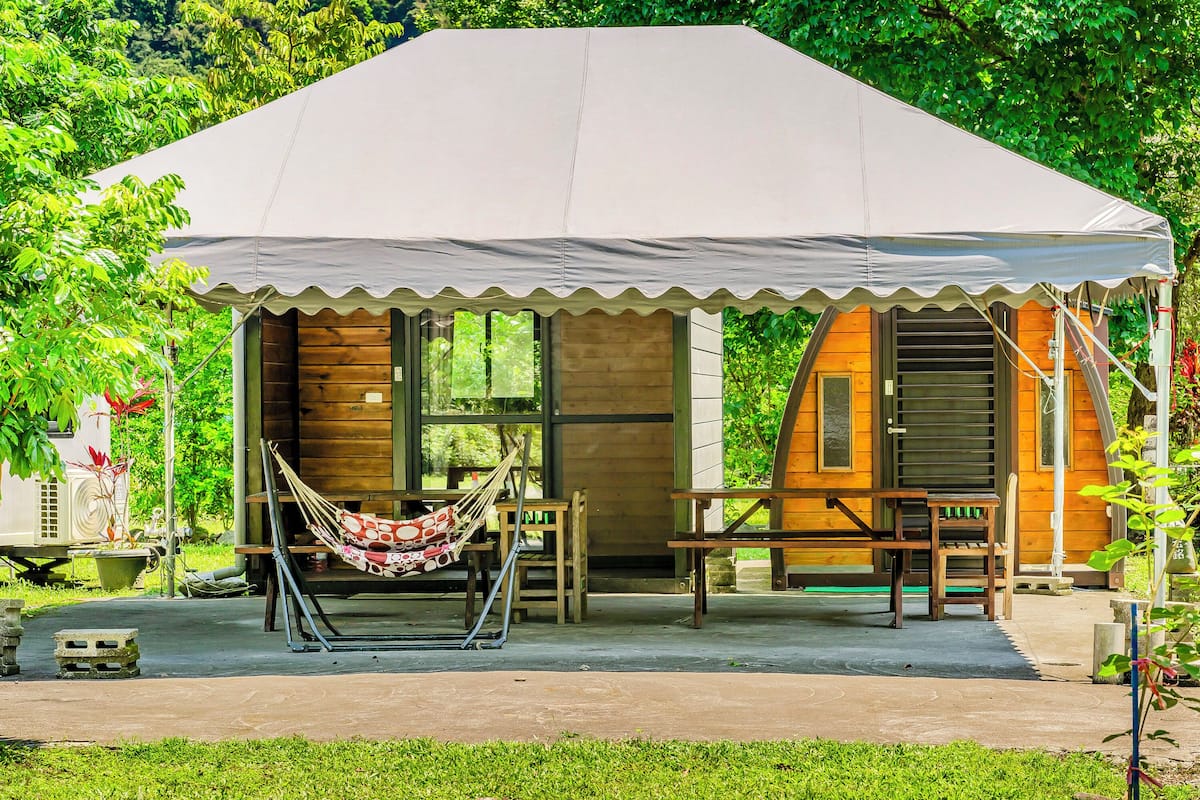 A small wooden cabin with a white canopy, a hammock, and a picnic table.