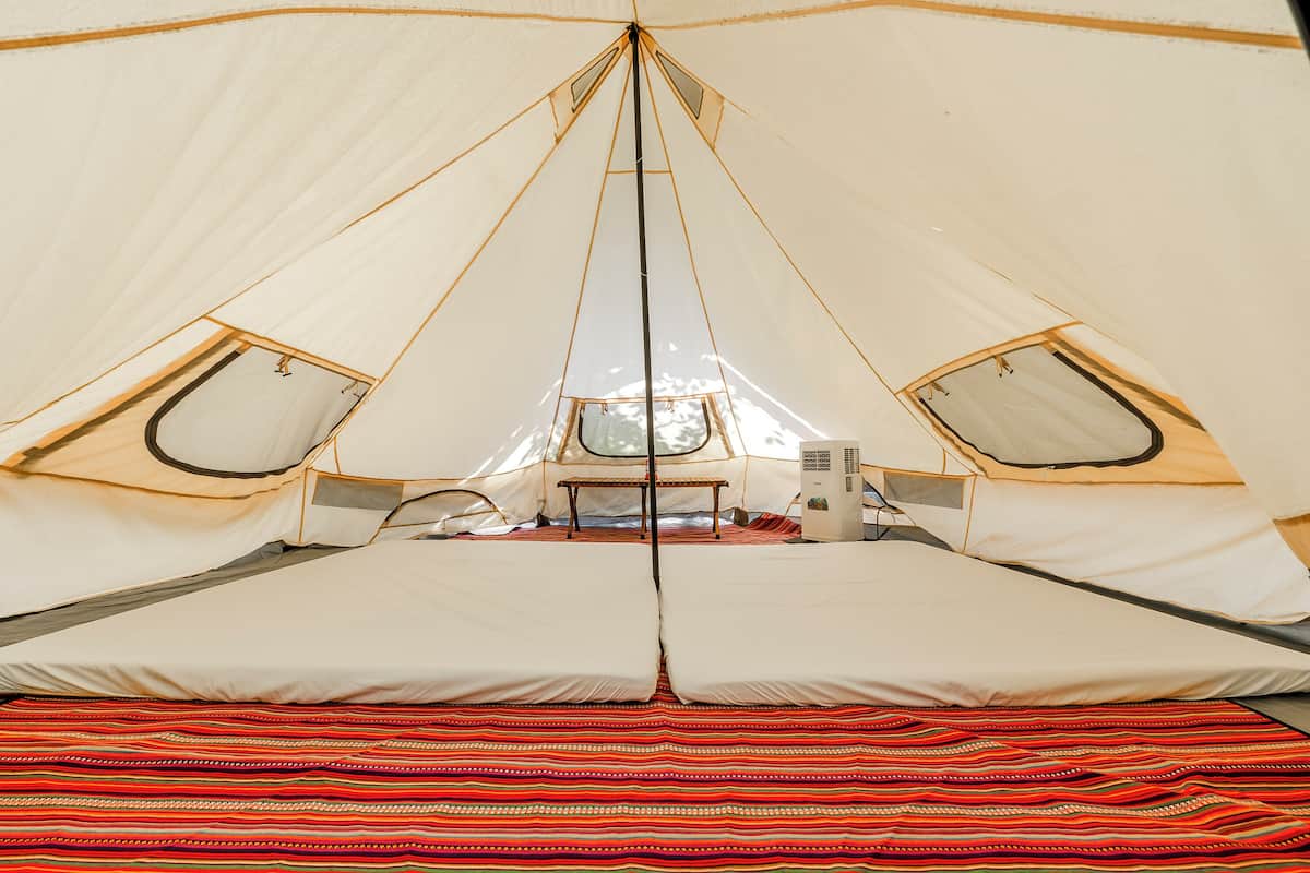 A tent with a central bed, two windows, and a table with chairs.