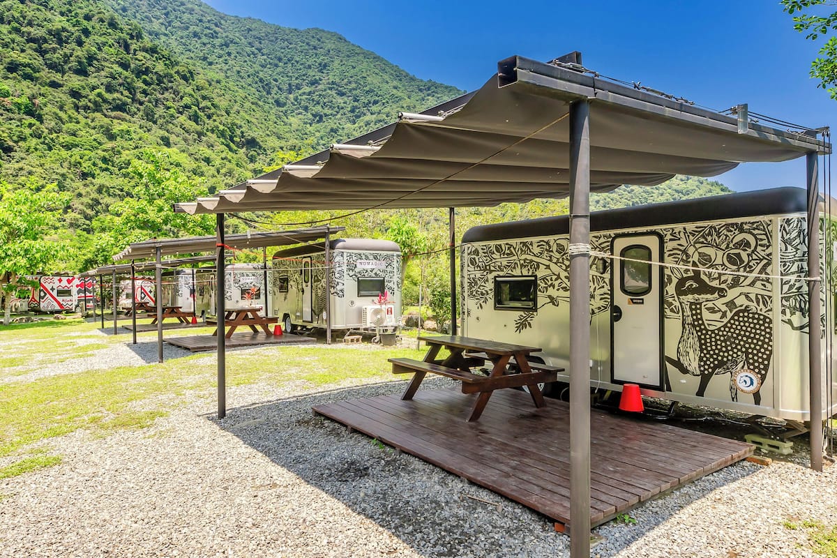 A campsite with picnic tables and a covered area, set against a mountainous backdrop.