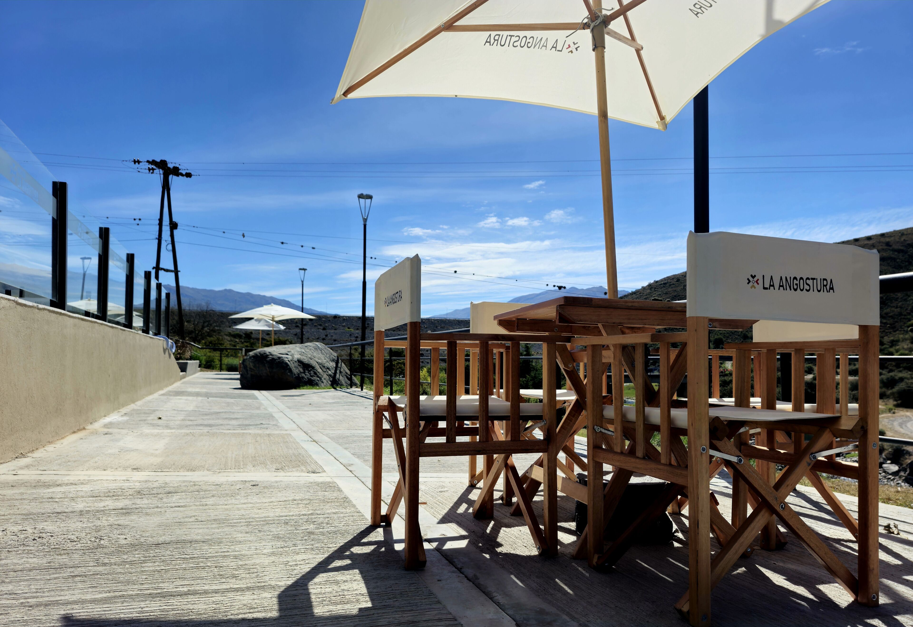 Outdoor wooden chairs and tables under a large umbrella, with a sign reading "LA ANGOSTURA".