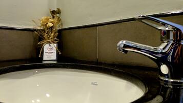 Un lavabo de baño con un lavamanos blanco, un grifo cromado y un pequeño jarrón con flores secas en la encimera.