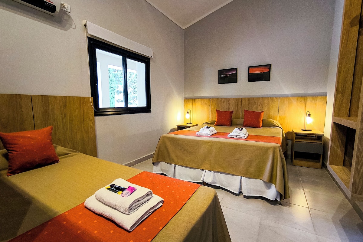 Une chambre d’hôtel avec deux lits, chacun doté d’une tête de lit en bois, d’une fenêtre et d’une table de chevet avec une lampe.
