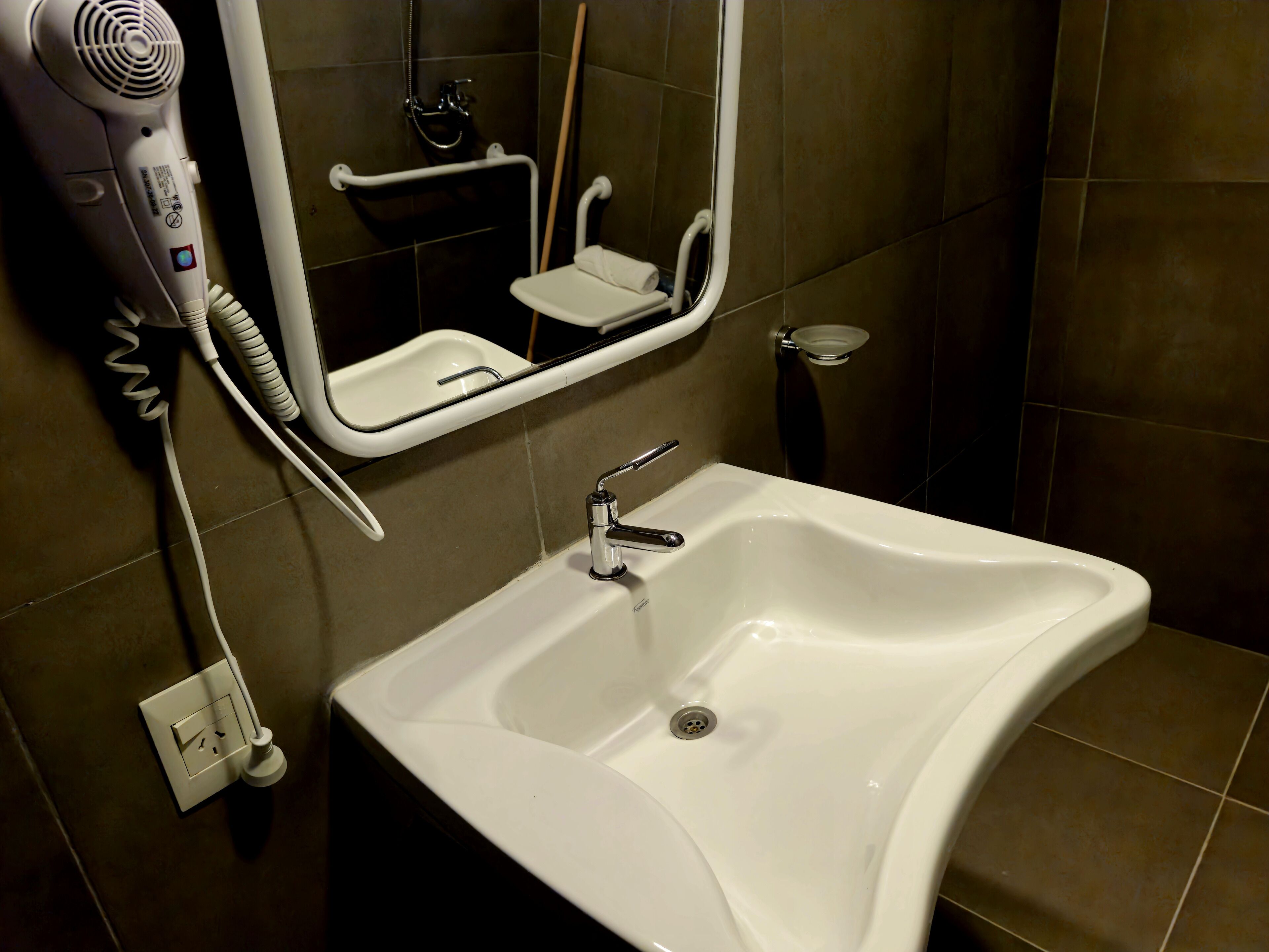 A bathroom with a white sink, a mirror, and a hairdryer on the wall.