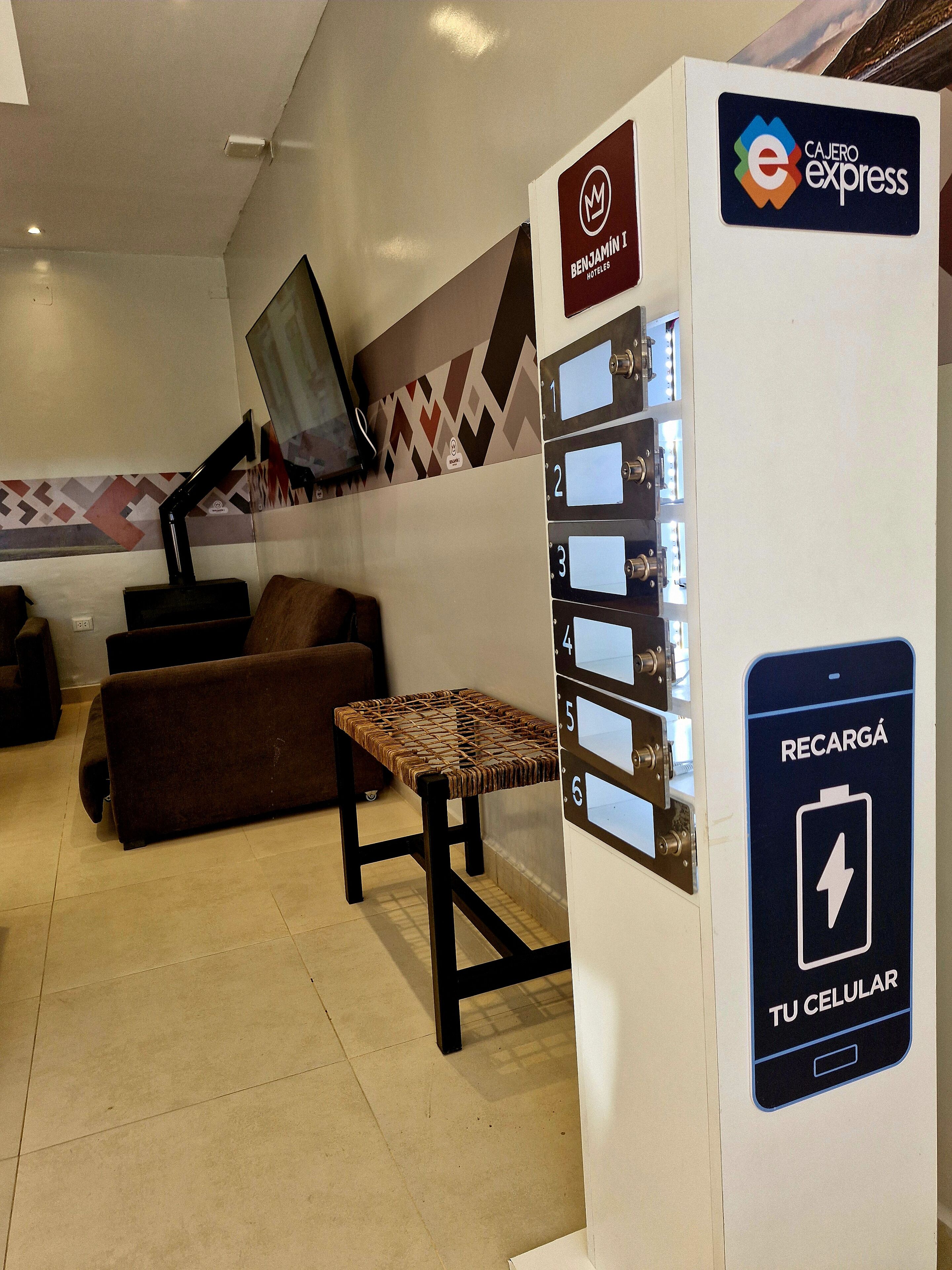 Zona de recepción de hotel con estación de carga para celular y televisor montado en la pared.