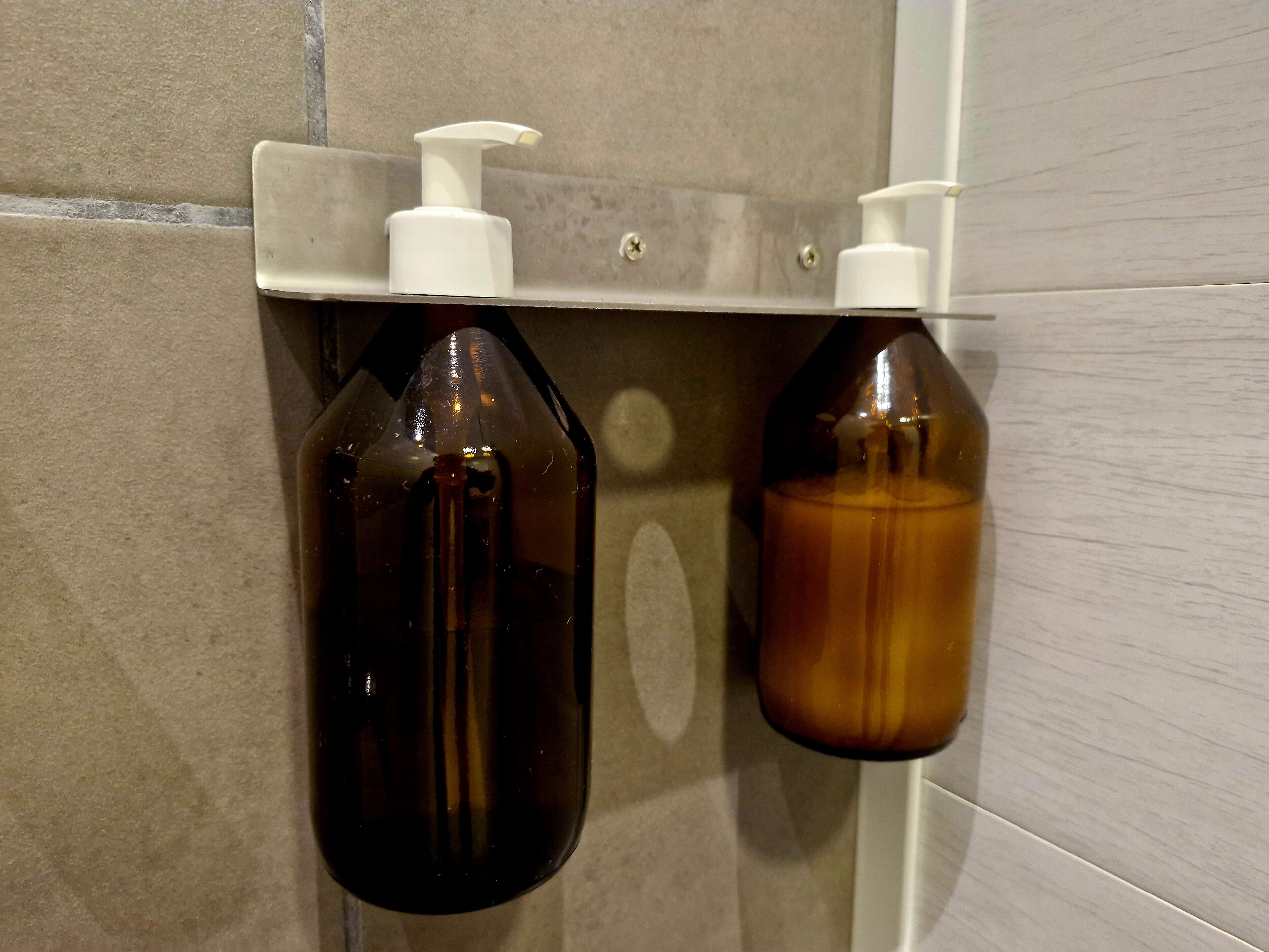 Un baño con dos botellas de jabón líquido fijadas a la pared.