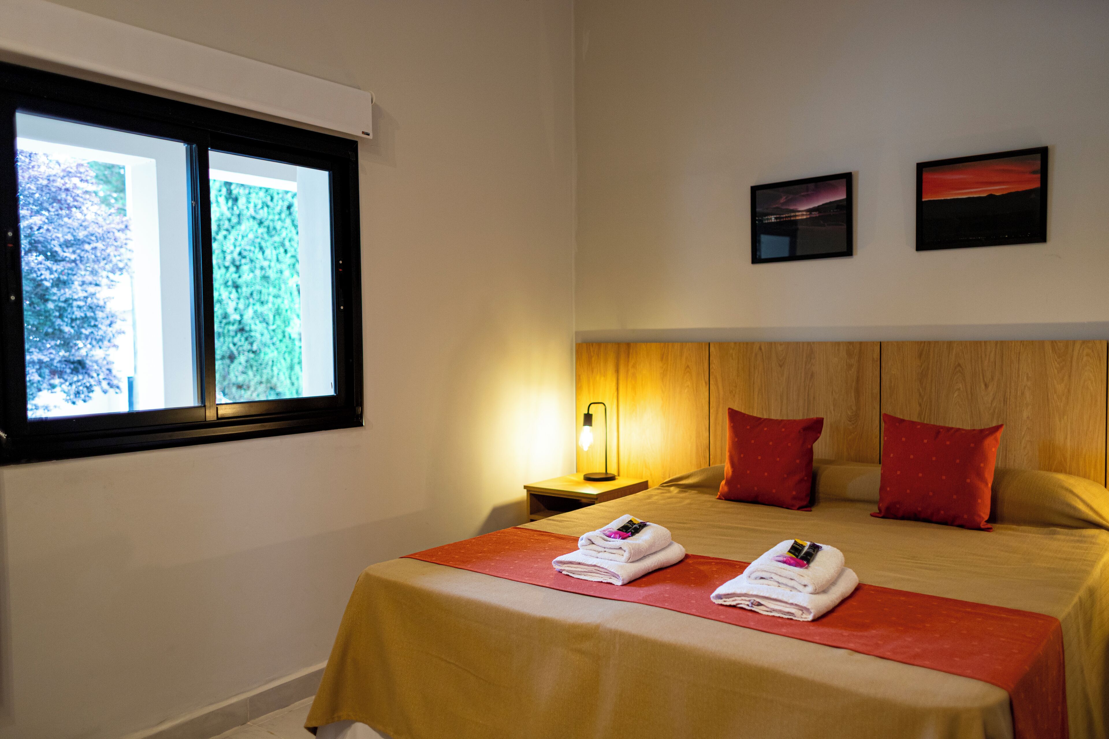 A hotel room with a bed, two pillows, a nightstand, a lamp, and two framed pictures on the wall.