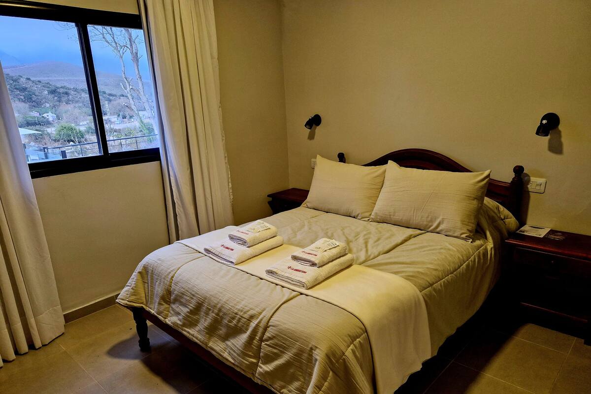 Un lit bien fait, avec des serviettes à portée de main, une fenêtre avec des rideaux et une vue sur un paysage.