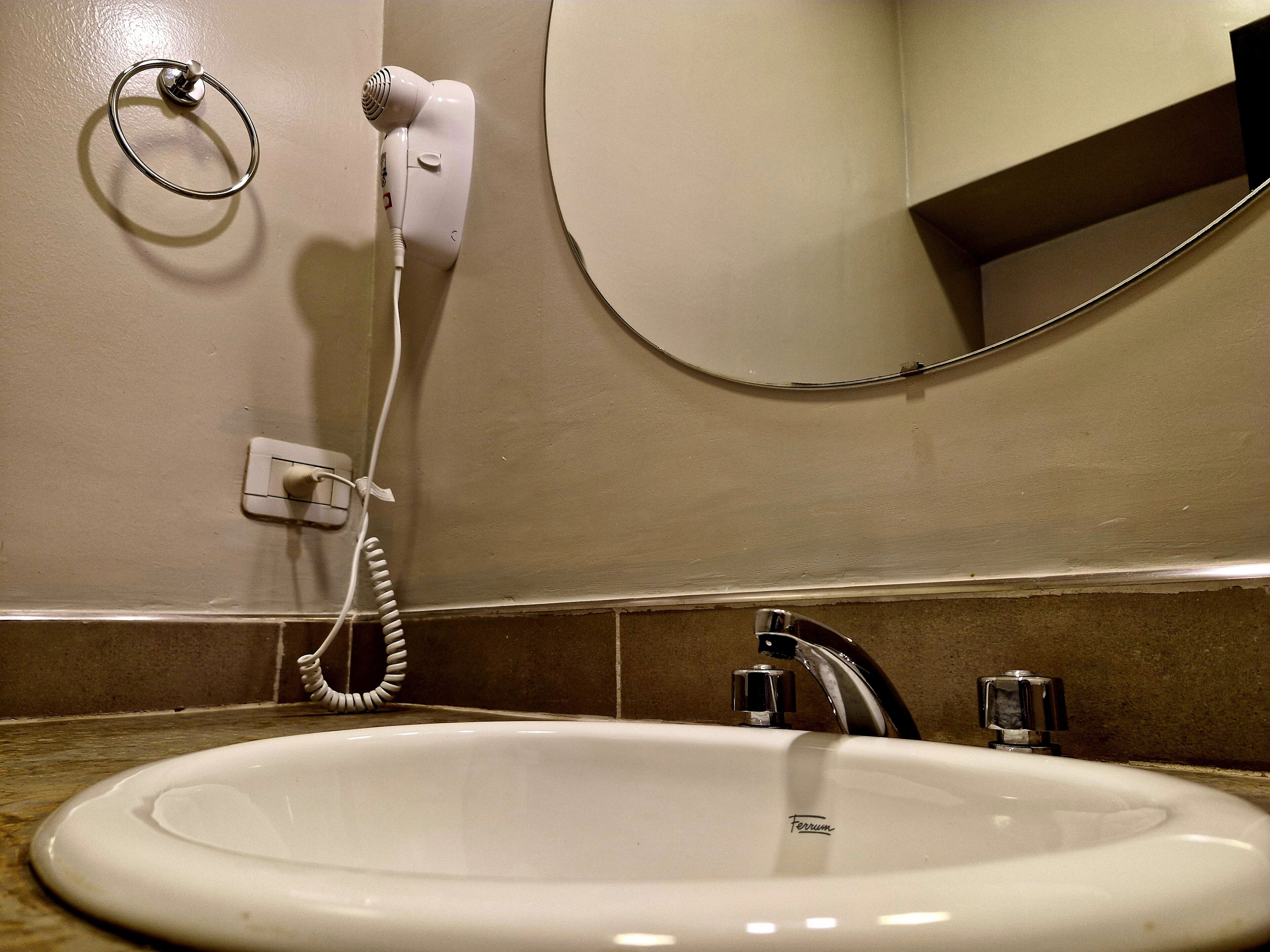 Un baño con un lavamanos blanco, un espejo y un secador de pelo conectado a la pared.