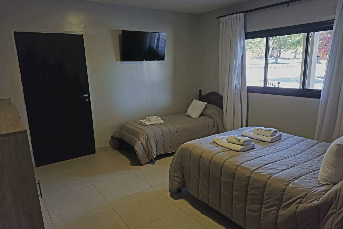 Une chambre d’hôtel avec deux lits, un téléviseur à écran plat fixé au mur, une fenêtre avec des rideaux et une porte.