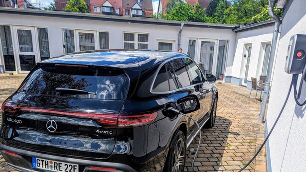 Un Mercedes-Benz GLC 400 noir, avec un câble de recharge branché à une borne de recharge fixée au mur.